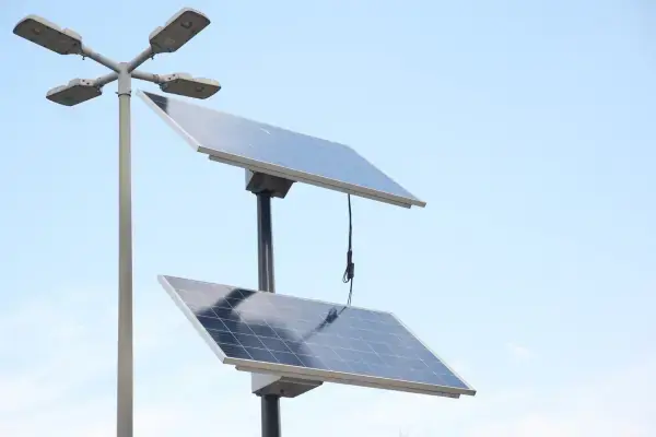 Dual-head solar street light with sun flare through the panel and a tree in the background